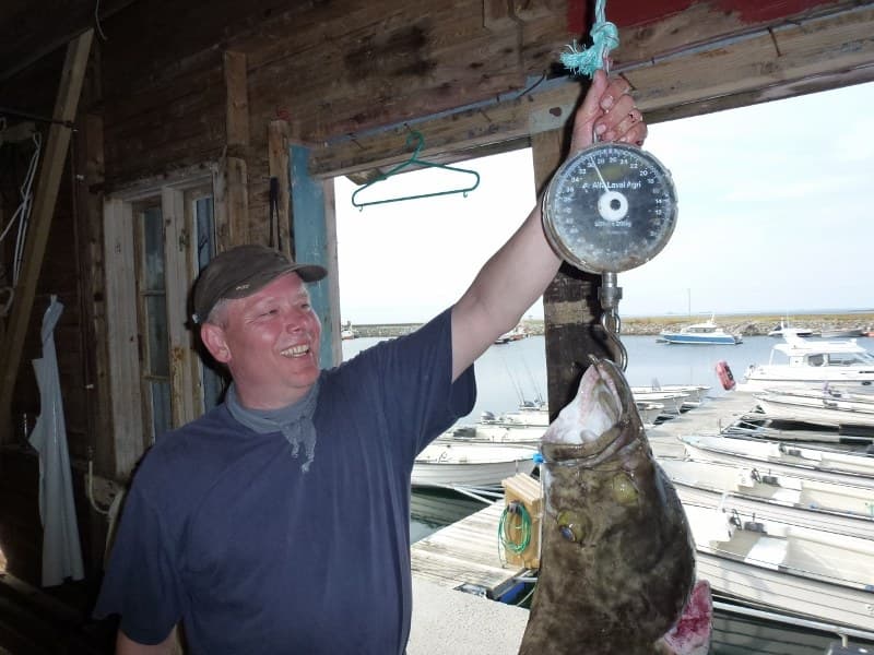Angler mit einem 30 Kilo schweren Heilbutt an der Waage im Bootshaus